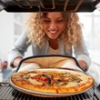 Mosolygós hölgy ahogy éppen kiveszi a friss ropogós pizzát amely a sütőben a pizzakövön sült meg