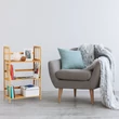 Natúr színű bambusz polc könyvekkel a nappaliban egy szürke fotel mellett elhelyezve