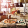 Frissen elkészült pizzát éppen felszeletelő pizzavágó olló egy vastag fa munkapulton