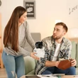 Fiatal pár ahogy egy fekete-fehér malacpersely tart a kezében a nappaliban