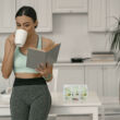 Teát szürcsölő hölgy háttérben egy fehér konyhával és egy teafilter tartóval