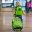 Sárkányos mintás hátizsákot viselő és gyermek bőröndöt húzó kissrác a repülőtéren