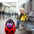 Katicabogara bőrönd mellett ülő gyermek a repülőtéren