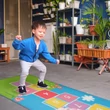 2 év körüli kisfiú, ahogy éppen egy ugróiskola mintás játékszőnyegen ugrál a gyerekszobában
