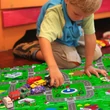 Összeállított puzzle játszószőnyeg egy város térképével díszített mintával és a rajta játszó kisfiúval