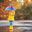 Sárga esőkabátban és gumicsizmában álldogáló kisláy kezében egy hercegnő mintás gyerek esernyő