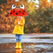 Szemből fényképezett esőben álló kislány kezében egy katicabogár mintájú gyerek esernyővel