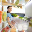 Egy hölgy ahogy éppen veszi ki a hűtőszekrényből a műanyag tojástartót