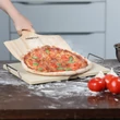 Vastag pizzakő és bambusz pizzalapát használat közben ahogy éppen lecsúszik róla a friss pizza