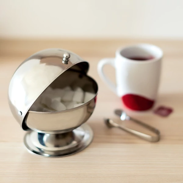 Frissen főzött bögre kávé mellett a konyhapulton elhelyezett rozsdamentes acél cukortartó gömb