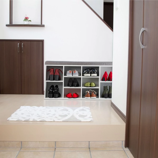 A beltéri emeletre vezető lépcső mellett elhelyezett fehér színű cipőtárolós ülőpad különböző színű cipőkkel