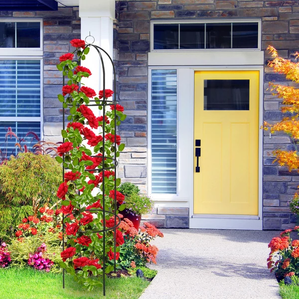 A bejárat előtt az előkertben elhelyezett piros színű rózsákkal felfuttatott rózsafuttató keret és növénytámasz