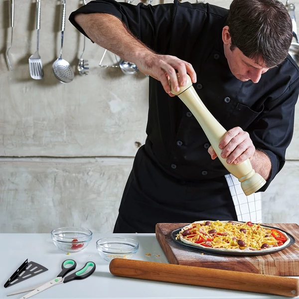 pizzaszakács ahogy az utolsó simításokat végzi egy éppen készülő pizzán a mellette elhelyezett pizzavágó olló készlettel