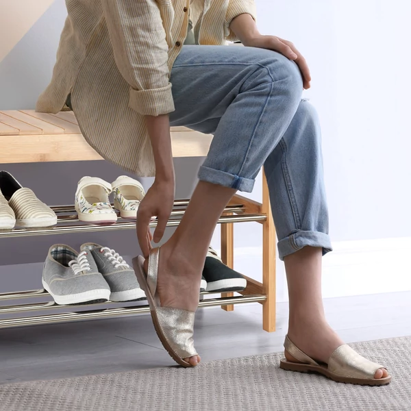 Egy bambusz cipőtartón ülő hölgy amint éppen a cipőjét veszi fel a lábára