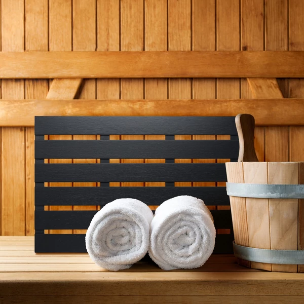 Longa fekete színű bambusz szaunaszőnyeg fehér törölközőkkel és vízesvödörrel egy szaunában