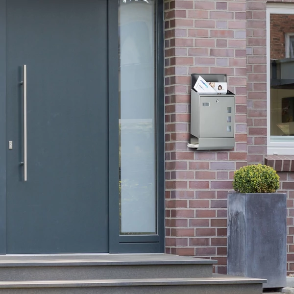 Modern szürke bejárati ajtó mellett a falon elhelyezett rozsdamentes acél kültéri postaláda 