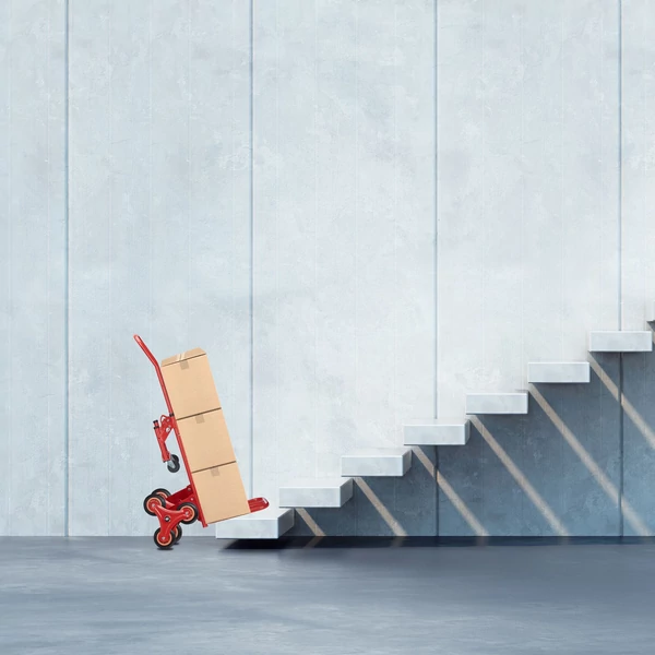 Dobozokkal felpakolt piros lépcsőzős molnárkocsi egy betonból készült lépcsősor előtt