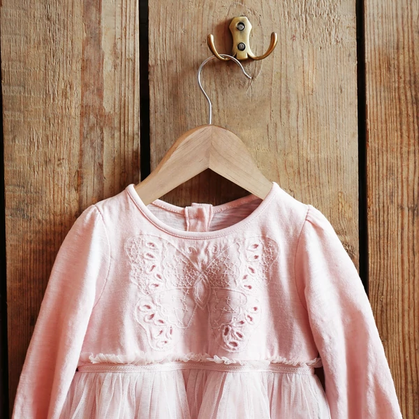 Rózsaszín kislány ruha egy fából készült natúr színű gyerek vállfán egy fa előszobafalon