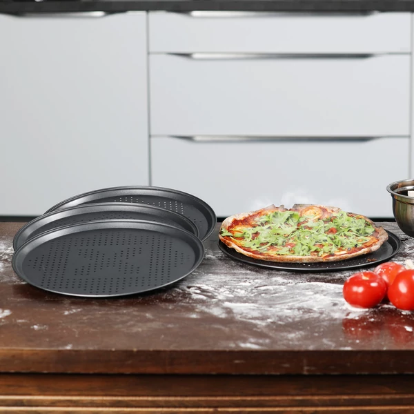 Perforált pizzasütő tálca készlet négy darab elemmel a konhyapulton éppen pizzkészítés közben
