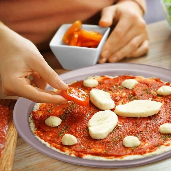 Barna színű pizzasütő forma amin egy készülő pizzát állítanak össze