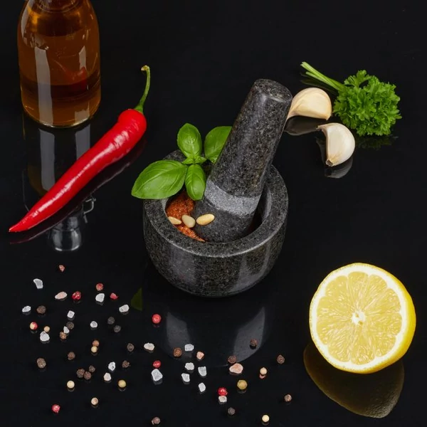 Kisméretű gránit mozsár és mozsártörő citrommal, fokhagymával és fűszerekkel körülvéve