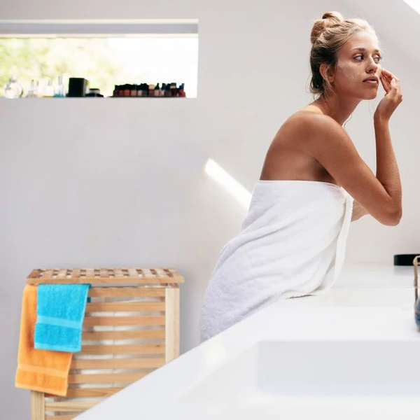 Ava natúr színű diófából készült szennyestartó a fürdőszobai ablak alatt kék és narancssárga törölközőkkel