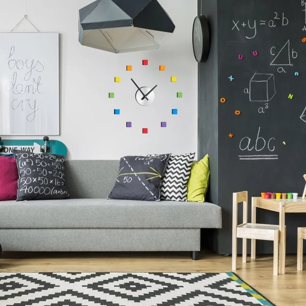 Szürke kanapé felett a fehér falon elhelyezett színes ragasztható nagyméretű falióra 