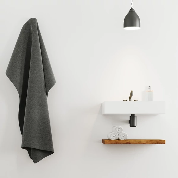 Minimal design fürdőszoba fali mosdóval alatta elhelyezett polccal sötétszürke fürdőlepedővel és a modsón elhelyezett szappanadagolóval