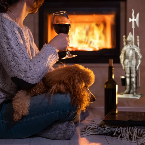 A kandallóban ropogó tűz mellett elhelyezett ezüst színű lovag alakú kandalló tisztító készlet