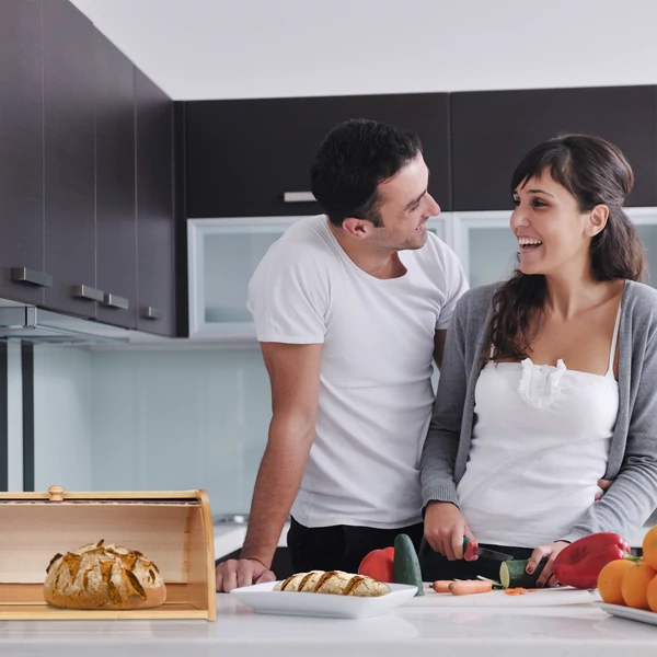 Konyhában reggelit készítő fiatal pár a bal oldalukon egy nyitott bambusz kenyértartóval több féle pékáruval