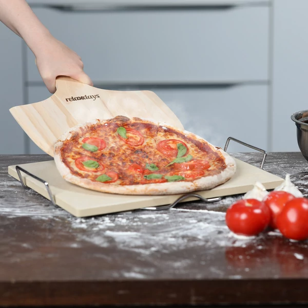 Vastag pizzakő és bambusz pizzalapát használat közben ahogy éppen lecsúszik róla a friss pizza