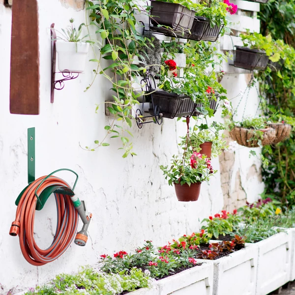 Zöld színű fali tömlőtartó és elektromos kábel tartó különböző fali virágtartók közé telepítve egy kerítésre